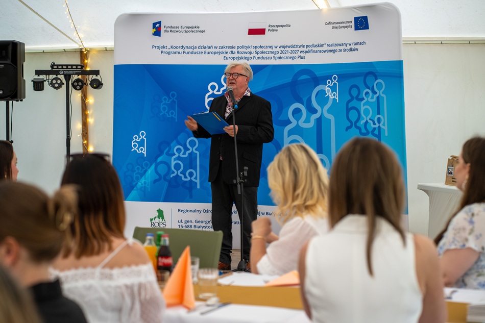 Zdjęcie przedstawia stojącego mężczyznę w sali konferencyjnej