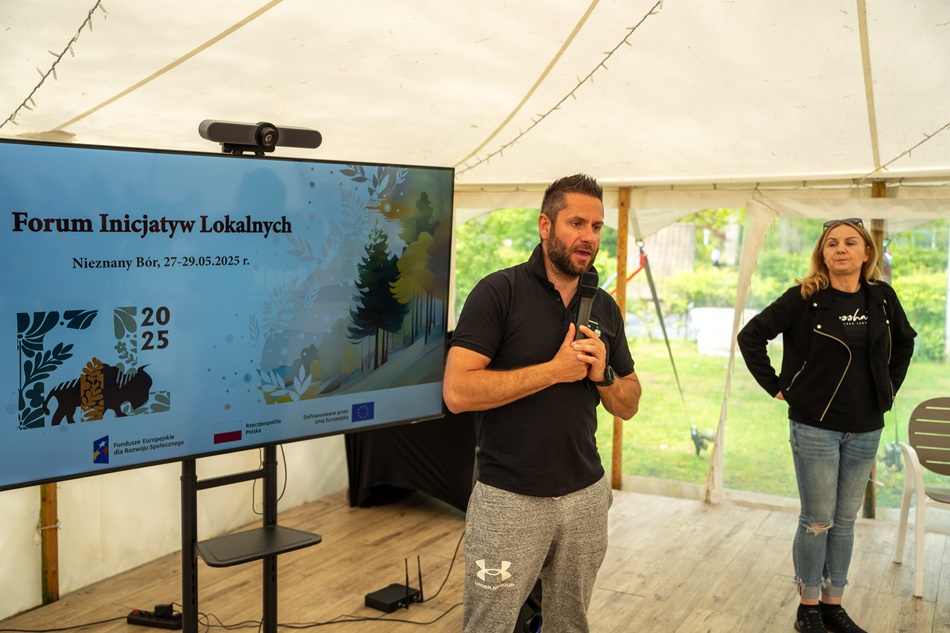 Zdjęcie przedstawia stojącego mężczyznę przemawiającego do mikrofonu