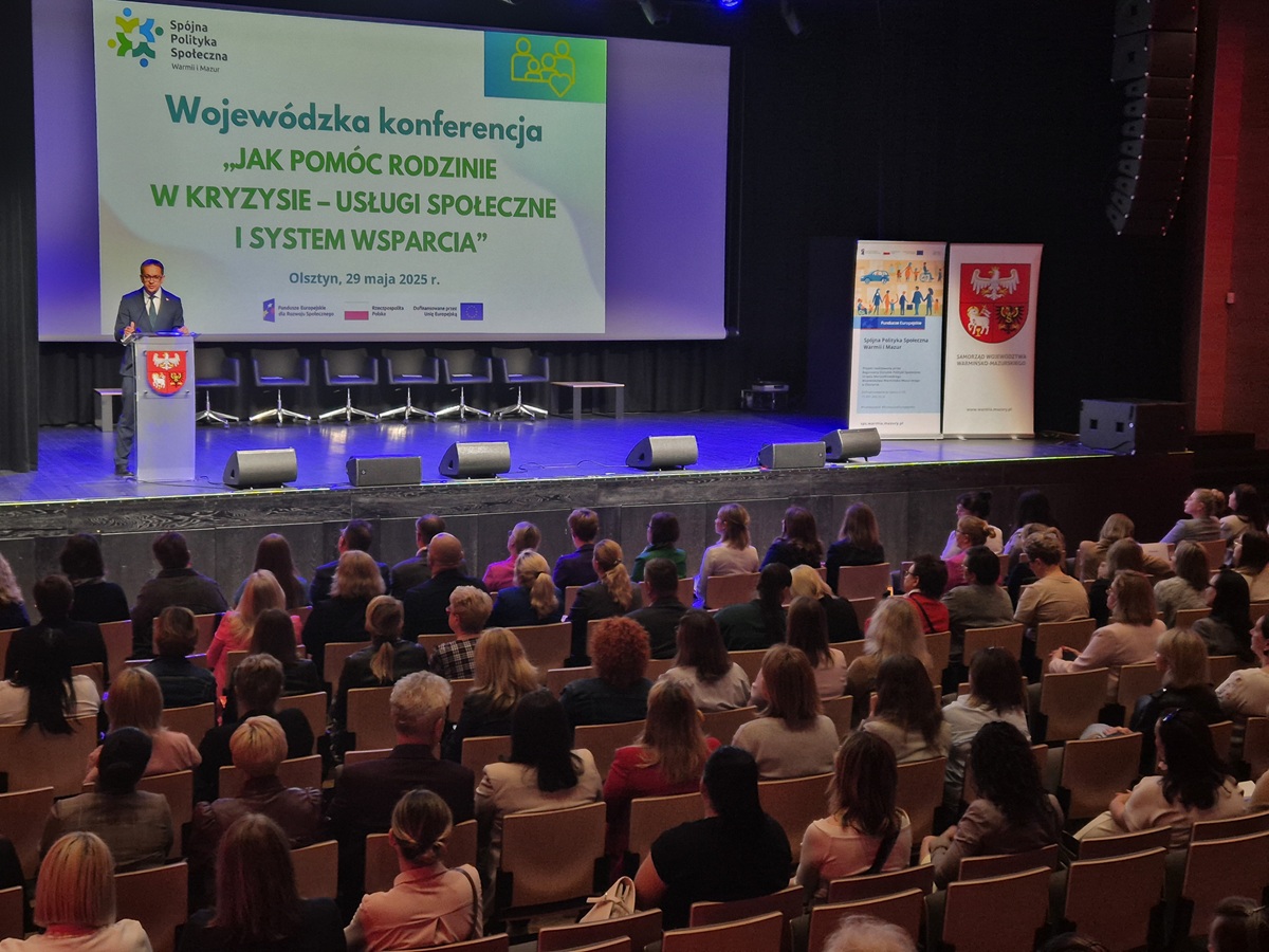 Zdjęcie przedstawia mężczyznę stojąca na scenie i przemawiająca w sali konferencyjnej
