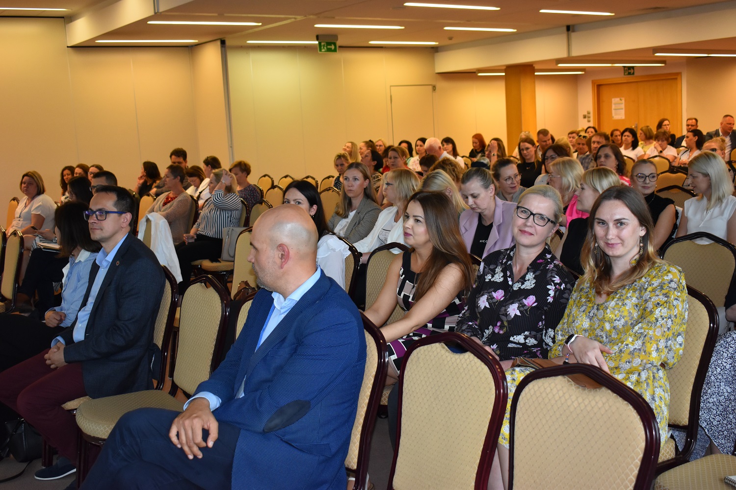 Zdjęcie przedstawia osoby siedzące w sali szkoleniowej zarówno kobiety jak i mężczyzn
