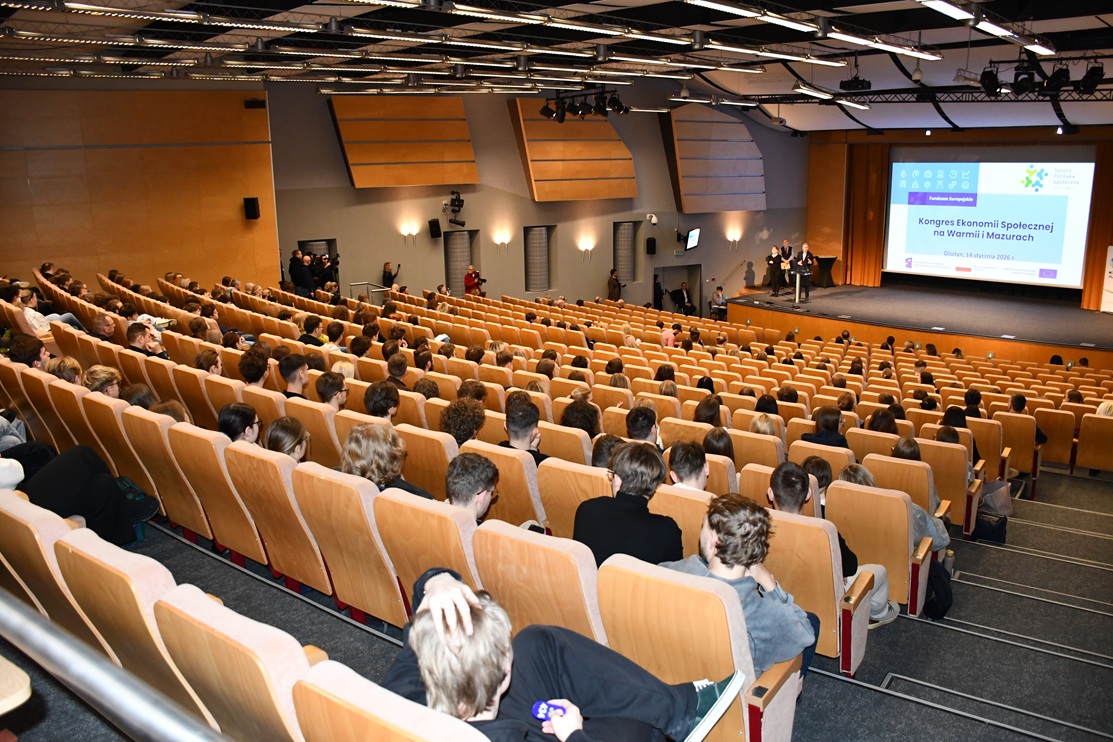 Zdjęcie przedstawia osoby siedzące w sali konferencyjnej zarówno kobiety jak i mężczyzn