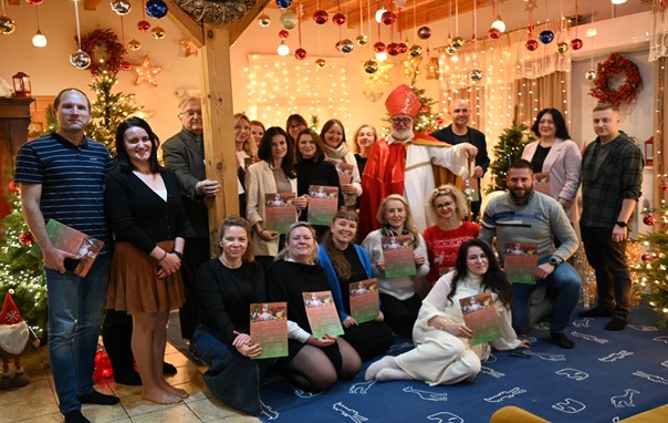 Zdjęcie przedstawia osoby stojące w jakimś pomieszczeniu  w tym kobiety i mężczyznę w tle widać mężczyznę przypominającego Świętego Mikołaja