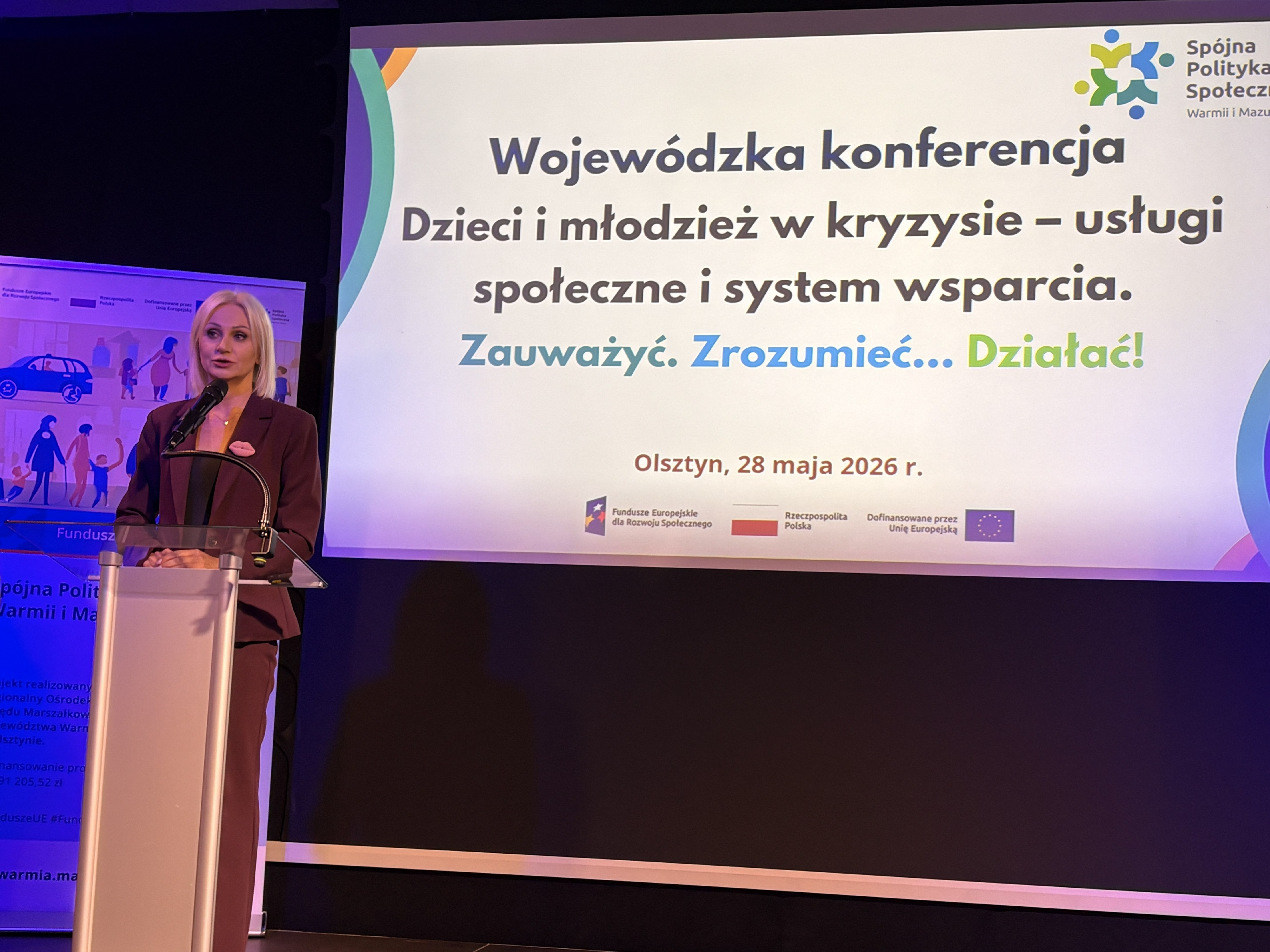 Zdjęcie przedstawia Panią Wicemrszałek Katarzynę Sobiech przy mównicy. W tle widać ekran z włączoną prezentacją na której znajduje się tytuł konferencji
